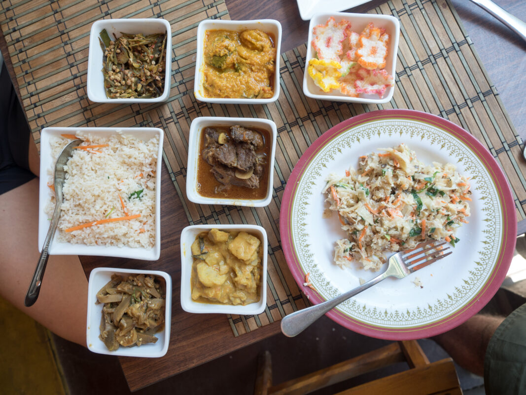 a table with a plate of rice and 8 different sri lankan curries in small pottles