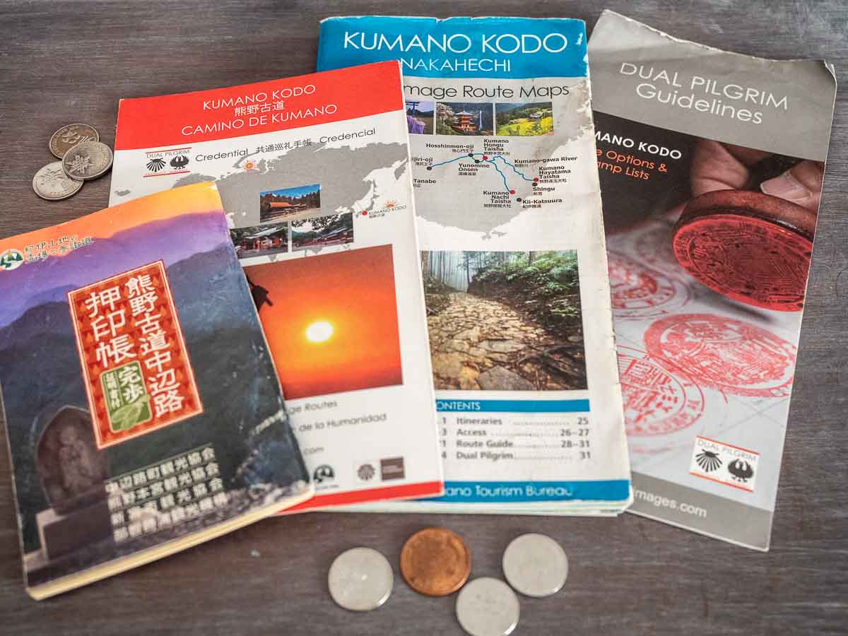 a pile of documents and maps for hiking the kumano kodo, along with a passport and some japanese yen coins