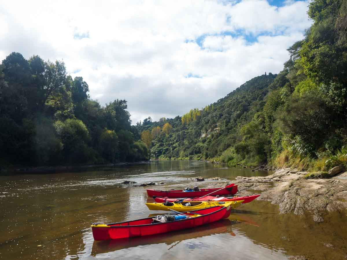Red and yellow canoes pulled onto a quiet Whanganui River bank