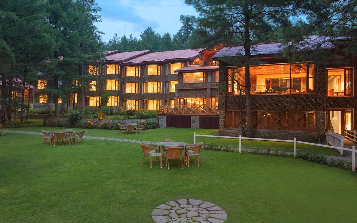 Welcomhotel Pine N Peak in Pahalgam lit up among pine trees at dusk